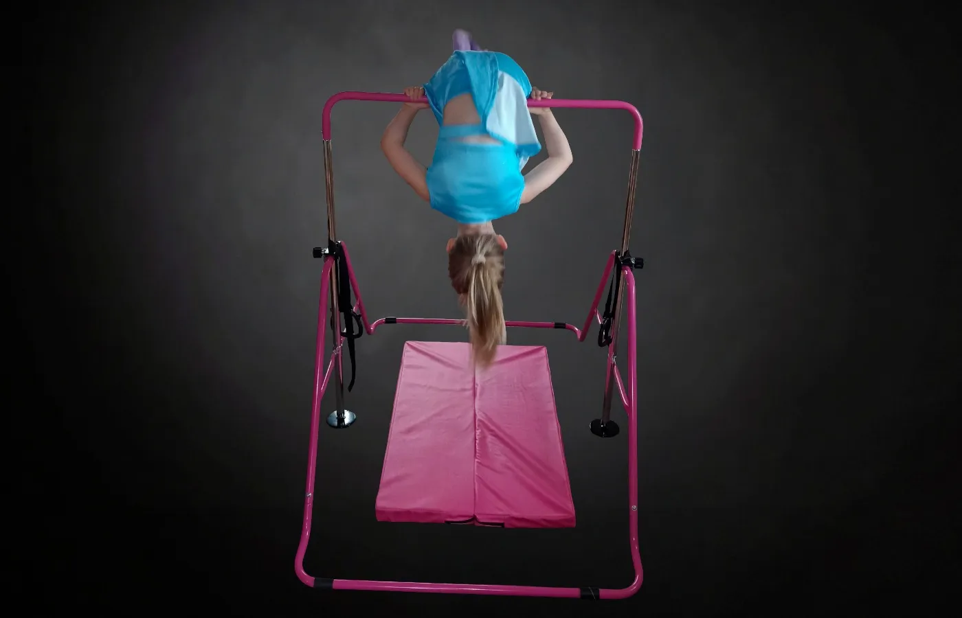 Mädchen turnt kopfüber an einem pinken Indoor-Turnreck für Kinder über einer Gymnastikmatte